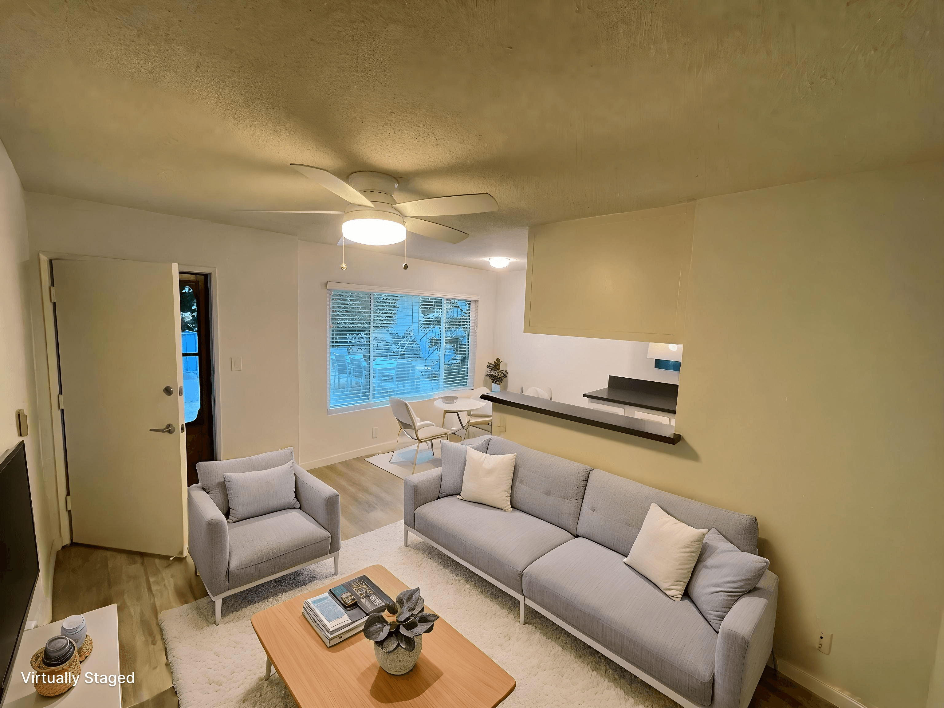 A living room with a grey couch, a coffee table, and a window with blinds.